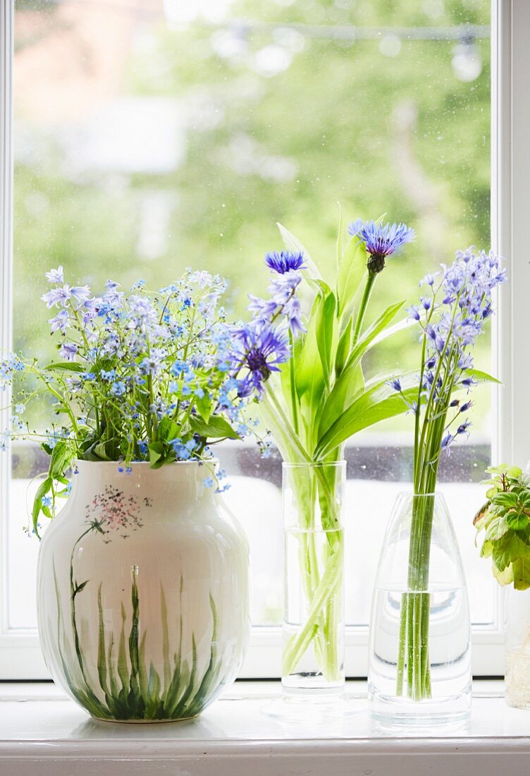 Three vases of delicate flowers on windowsill