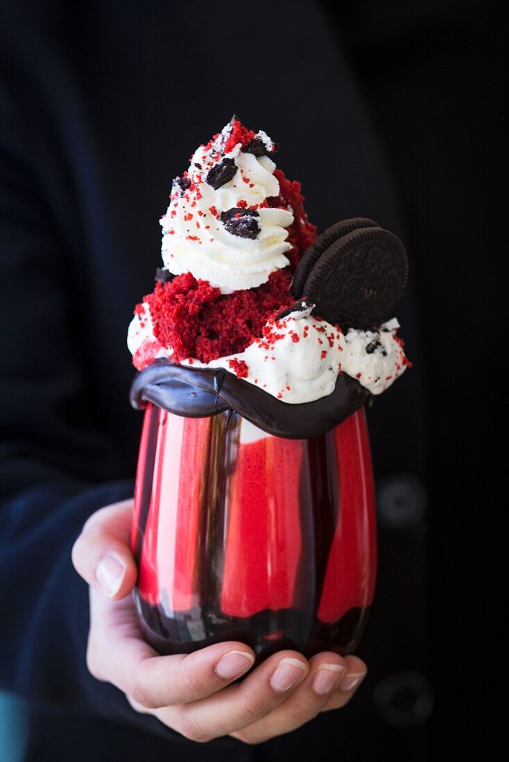 A woman holding a red velvet freak shake with Oreo biscuits
