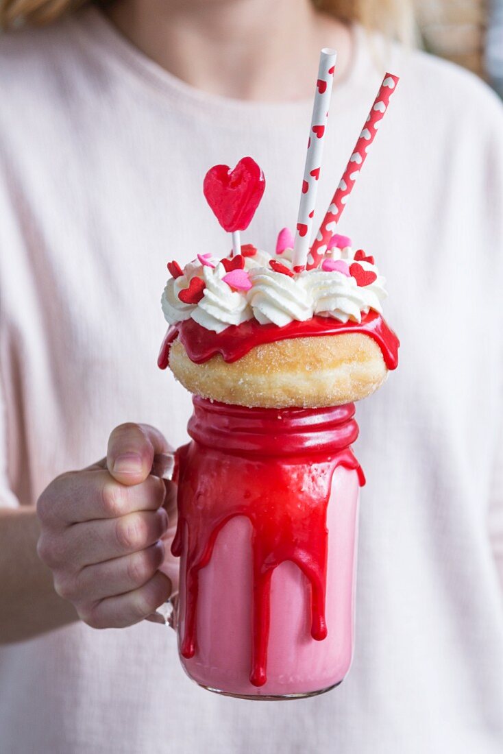 A woman holding a Valentine's freak shake with a mini doughnut and heart-shaped lollipop
