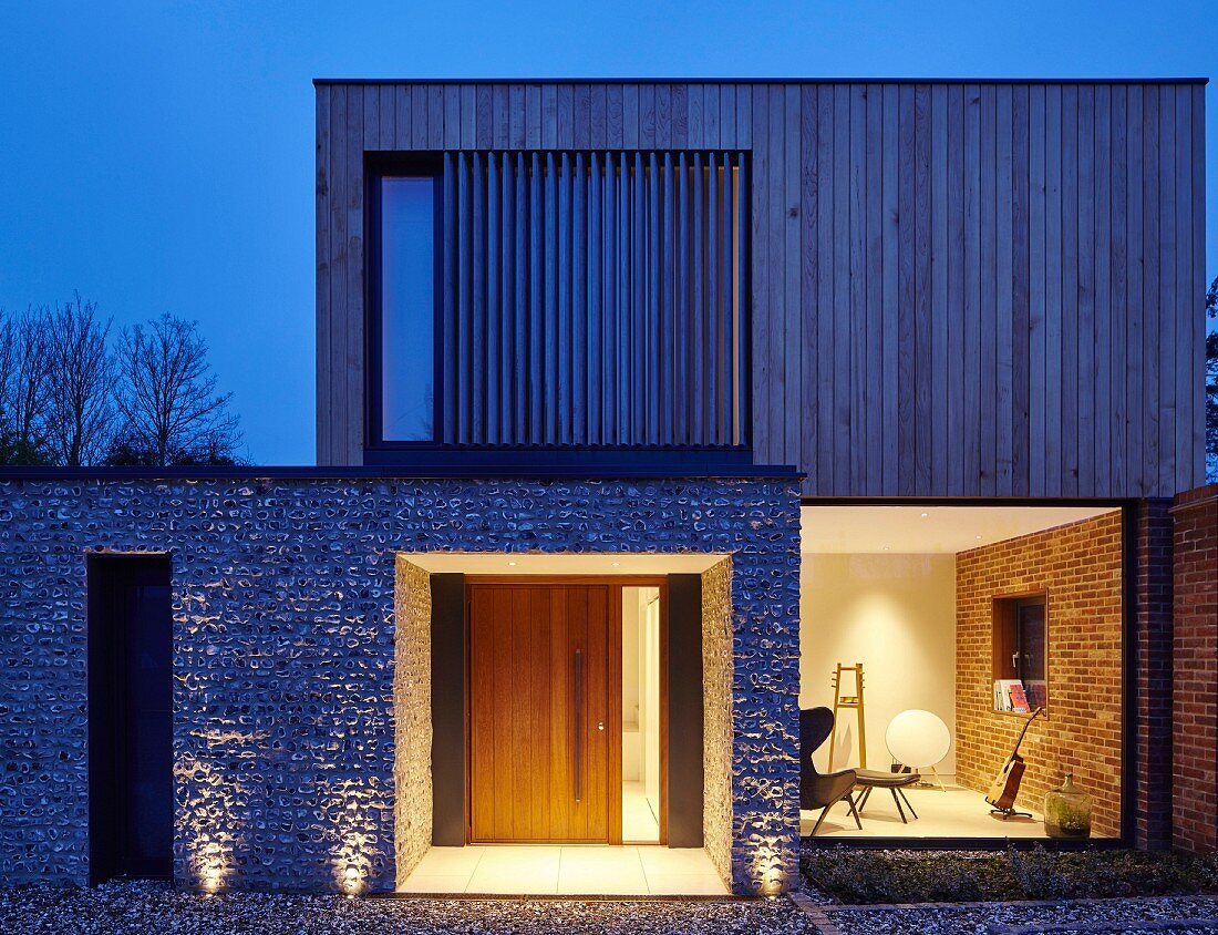 Kubisches Haus mit Fassade aus Holz und Stein bei Nacht