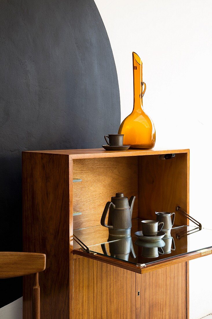 Retro-style cabinet with coffee set in fold-down cupboard against black circle on wall