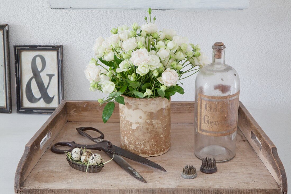 Strauß mit weißen Röschen neben alter Flasche und Vintagedeko