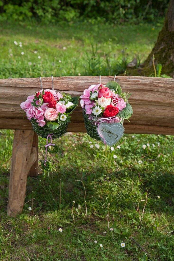 Two metal baskets filled with grass and flowers on wooden bench