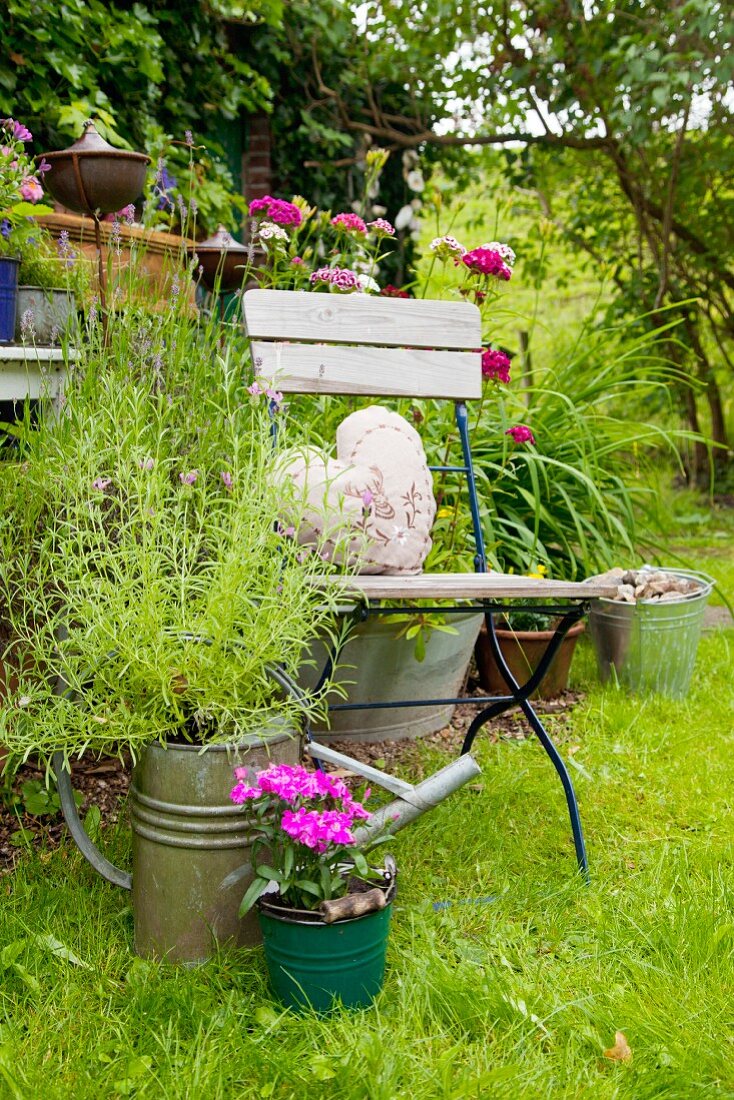 Flowering plants planted in watering can next to chair in garden