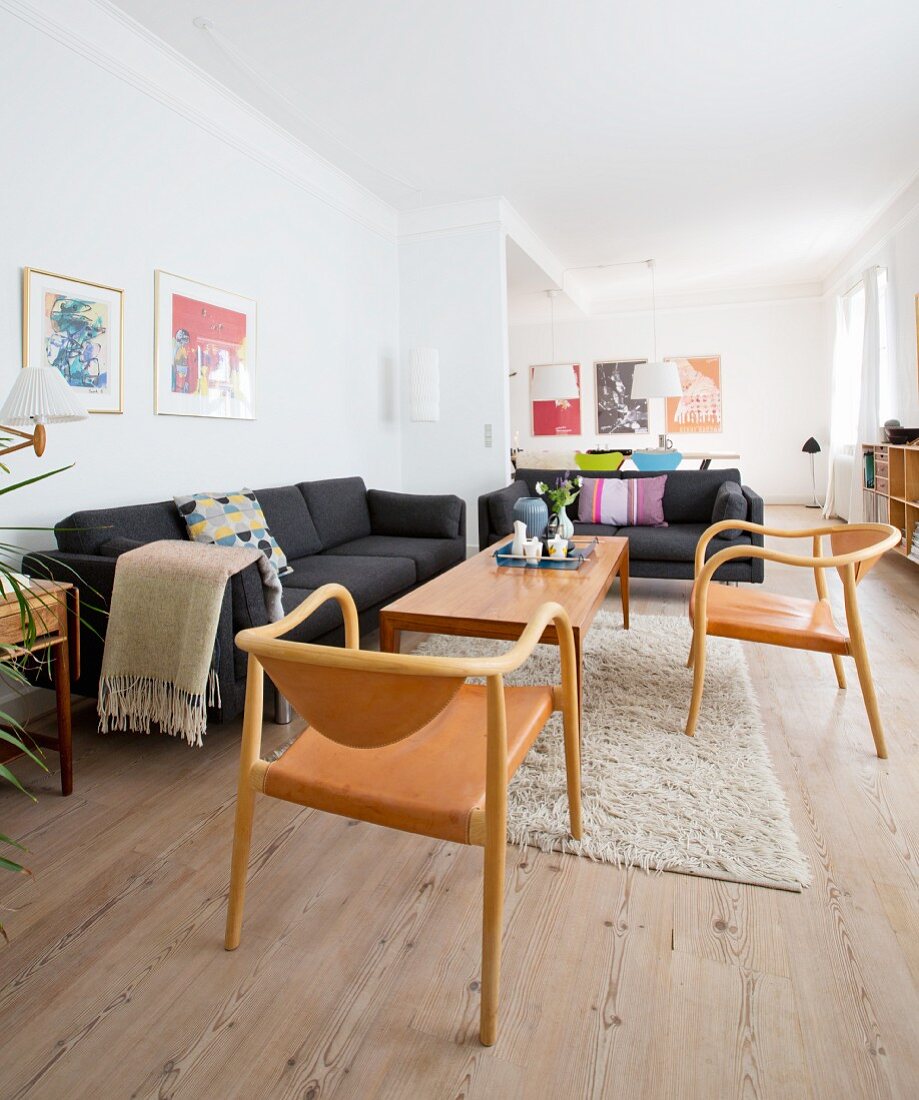 Offener Wohnraum mit Holzboden, schwarzen Sofas und Holz-Lederstühlen in renovierter Altbauwohnung