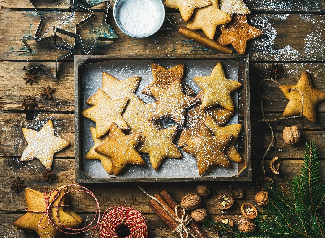 Gingerbread star shaped cookies in wooden tray, sugar powder, nuts, spices, baking molds