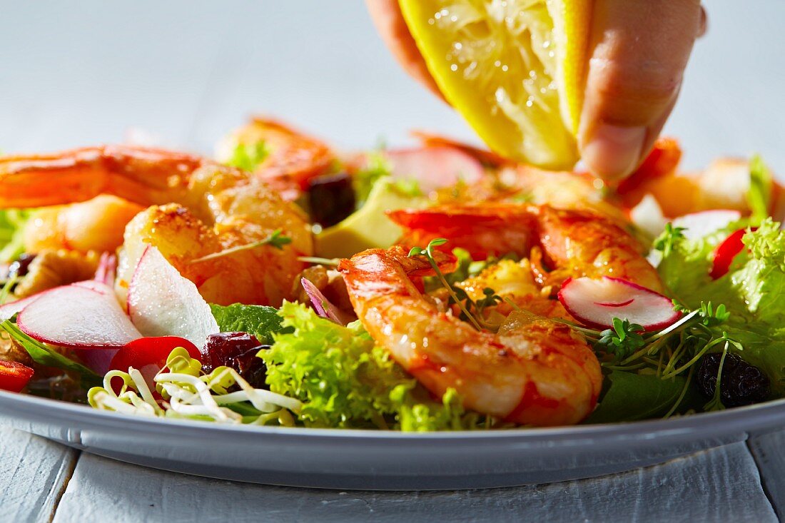Lemon juice being squeezed onto a prawn salad (close-up)