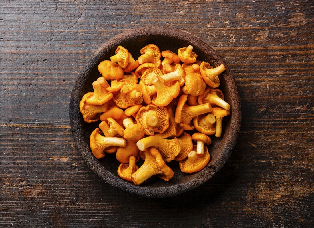 Fresh chanterelle mushrooms in a bowl on a wooden surface