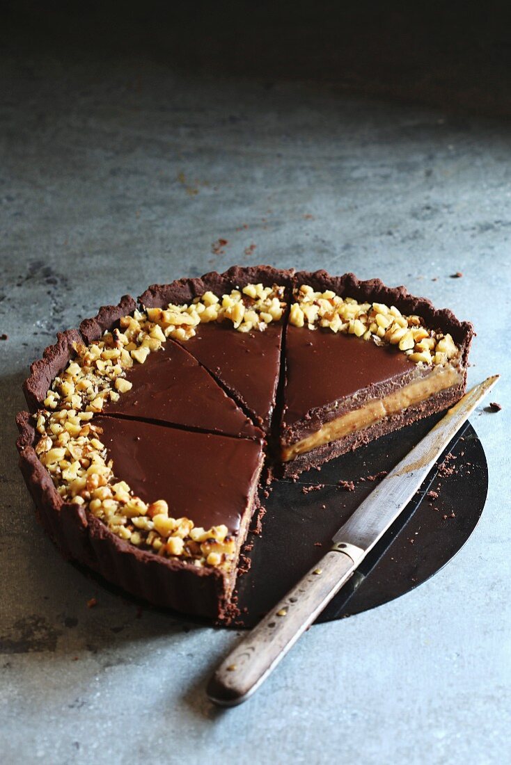 Sliced chocolate and caramel tart topped with walnuts