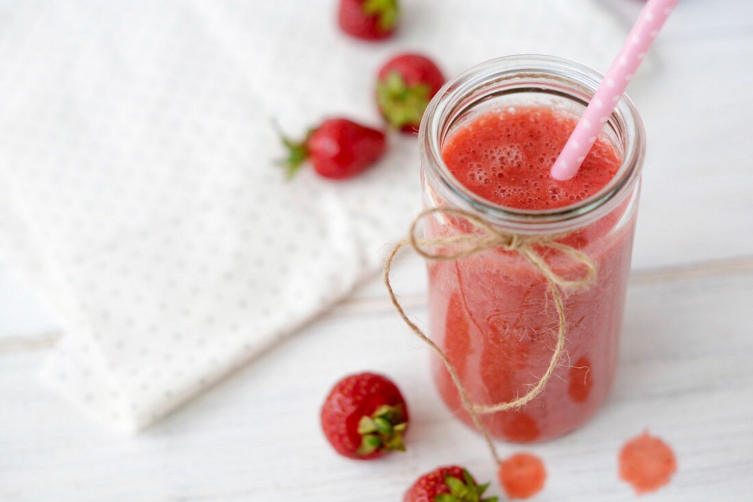 Strawberry, banana and orange smoothie in a glass jar with a straw