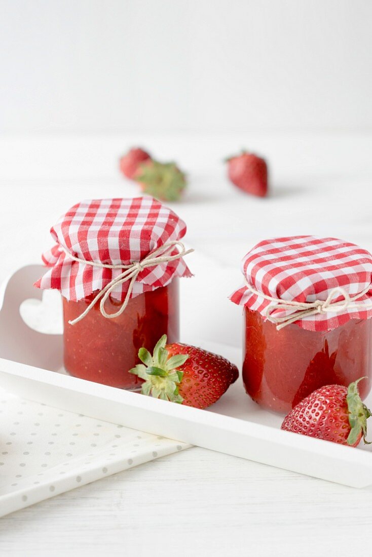 Two jars of strawberry jam on a tray