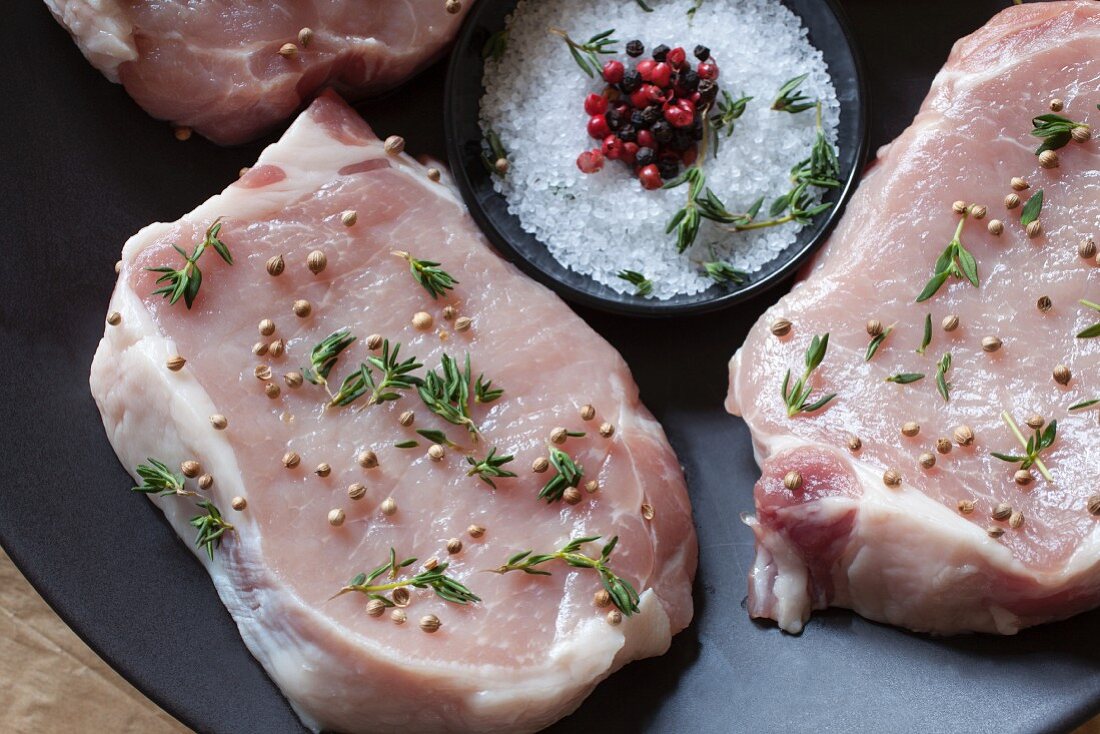 Raw pork chops seasoned with thyme, coriander, salt and pepper