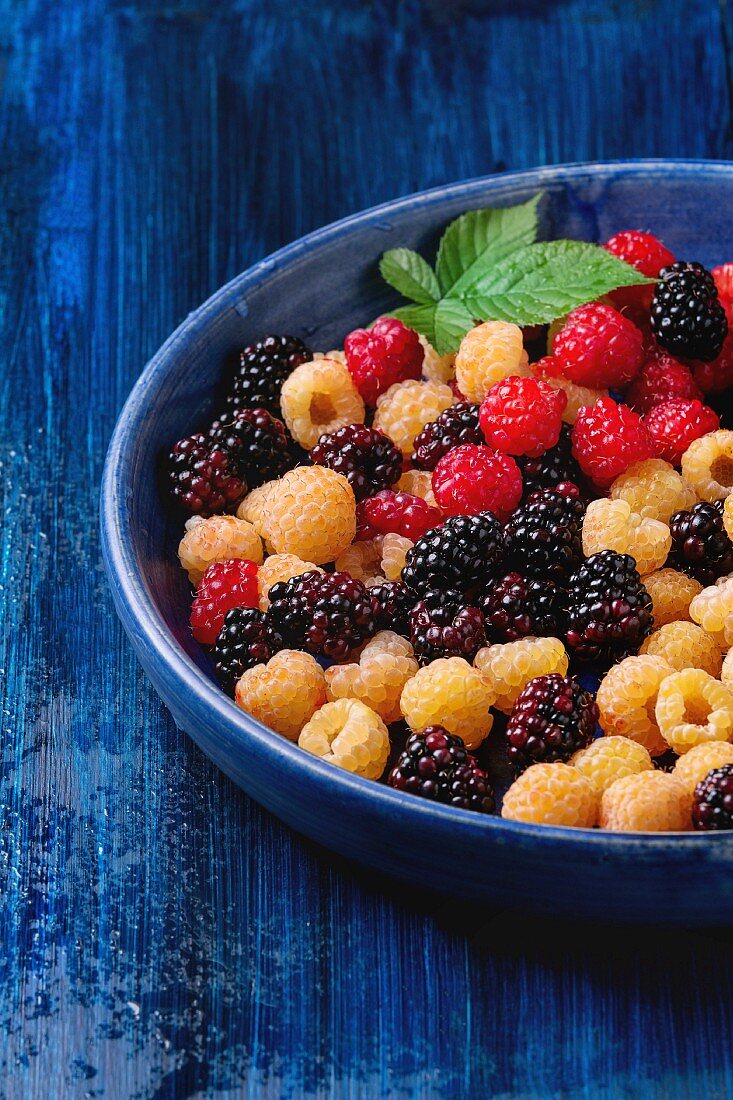 Blue ceramic plate of colorful yellow and red raspberries and black dewberry with leaf