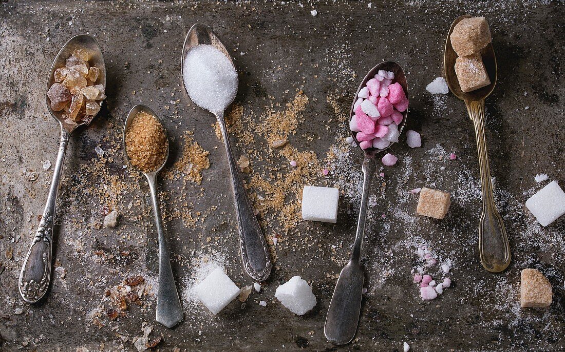 Different vintage spoons with variety of sugar white, brown pink fruit granulated, cubes and crystal