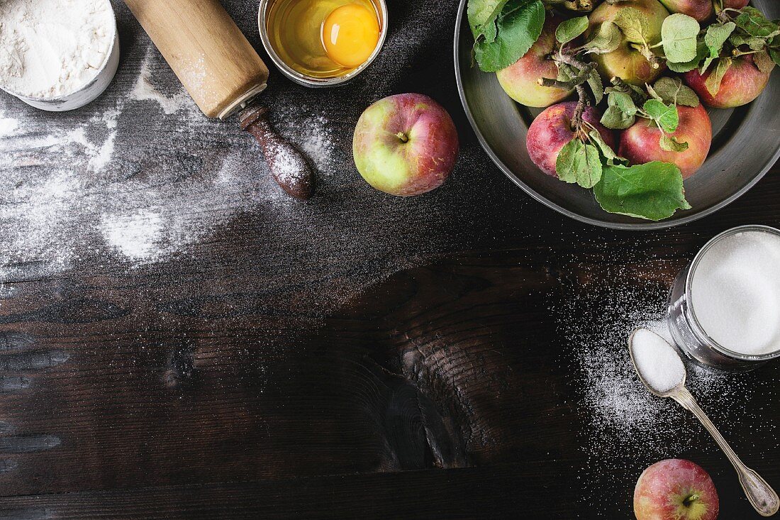 Zutaten für Apfelkuchen: Mehl, aufgeschlagenes Ei, frische Äpfel und Zucker, Nudelholz