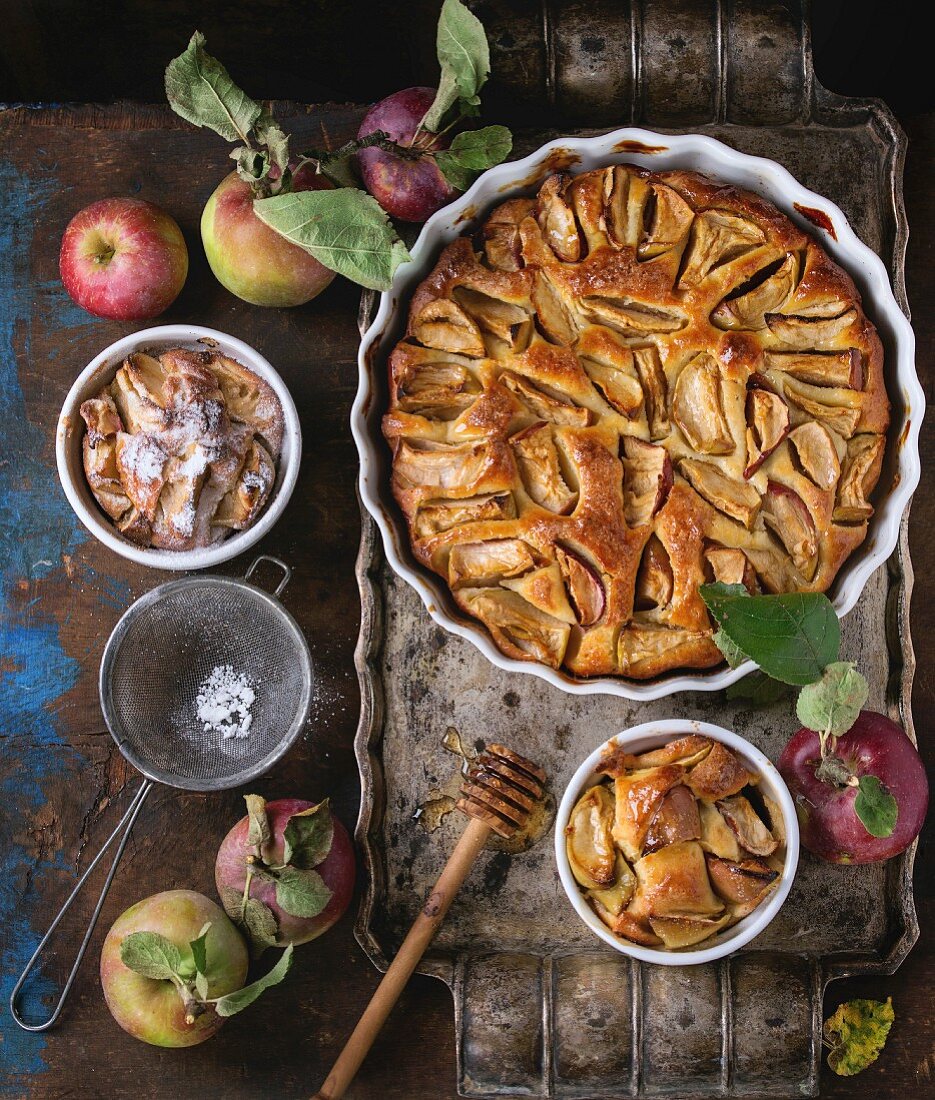 Apple cake in a white ceramic flan dish with fresh apples, honey and cinnamon sticks