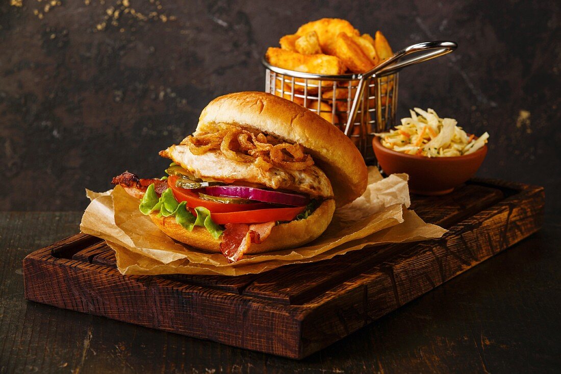 A burger with chicken breast and fried onions served with coleslaw and potato wedges