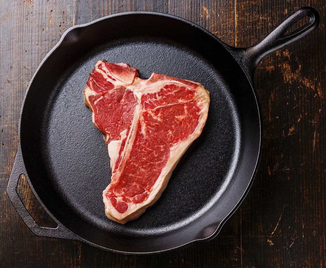 Raw fresh meat T-bone steak on cast iron frying pan on wooden background