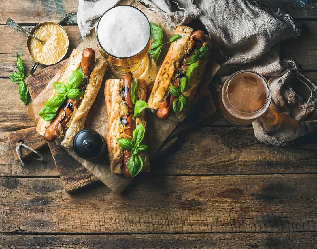 Glasses of wheat unfiltered beer and homemade grilled sausage dogs in baguette with mustard, caramelised onion and herbs