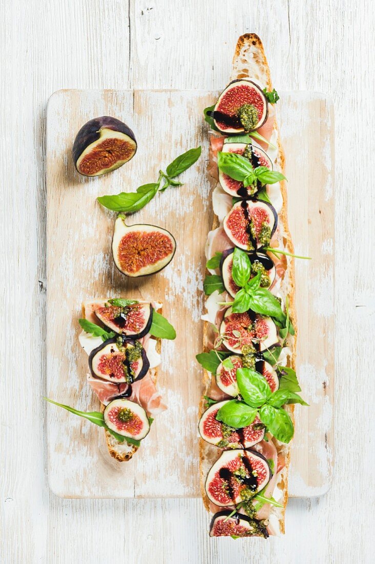 A baguette topped with ham, mozzarella, rocket, figs and basil on a wooden surface