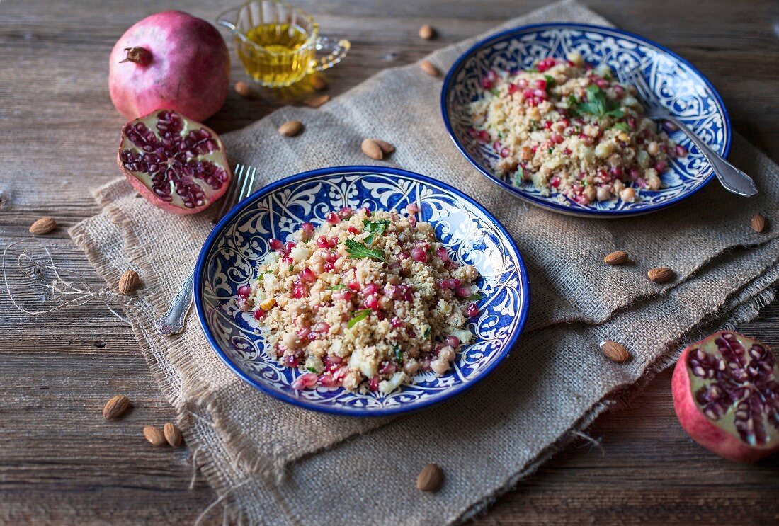 Couscous mit Kichererbsen, Mandeln und Granatapfelkernen auf blauen Keramiktellern