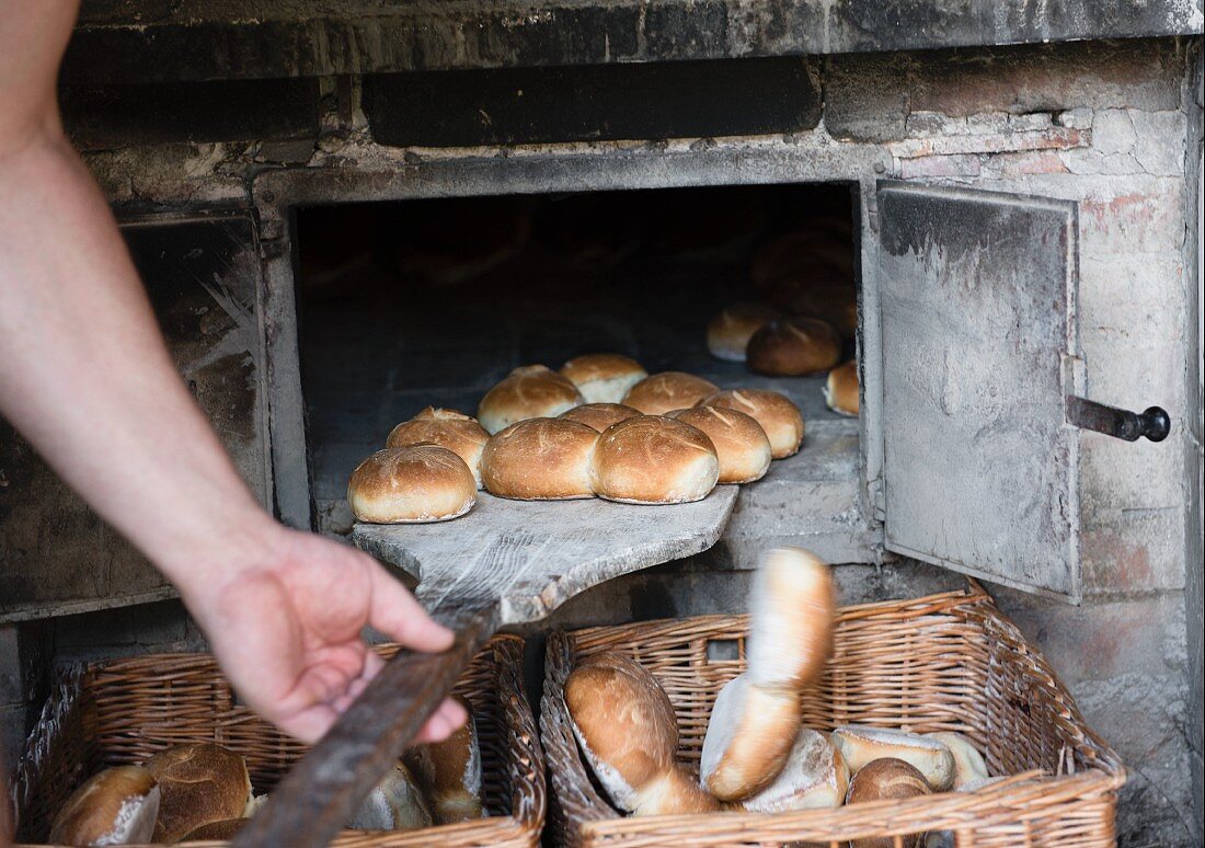 A man sliding bread rolls out of the oven and into wicker baskets