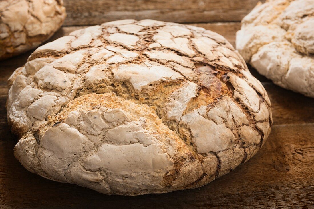 Large loaves of bread baked in a wood-fired oven on a wooden surface