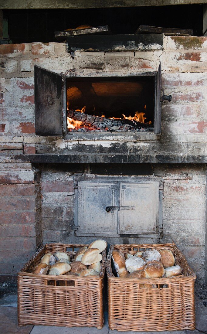 A glowing wood stove and freshly baked bread rolls in wicker baskets