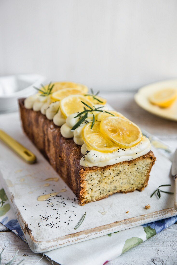 A lemon and poppy seed loaf with cream cheese frosting and rosemary syrup, with a slice removed