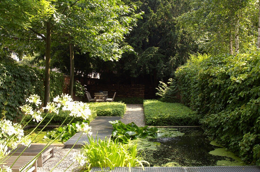 Garten mit Teich und Gittersteg, im Hintergrund schattiger Sitzplatz