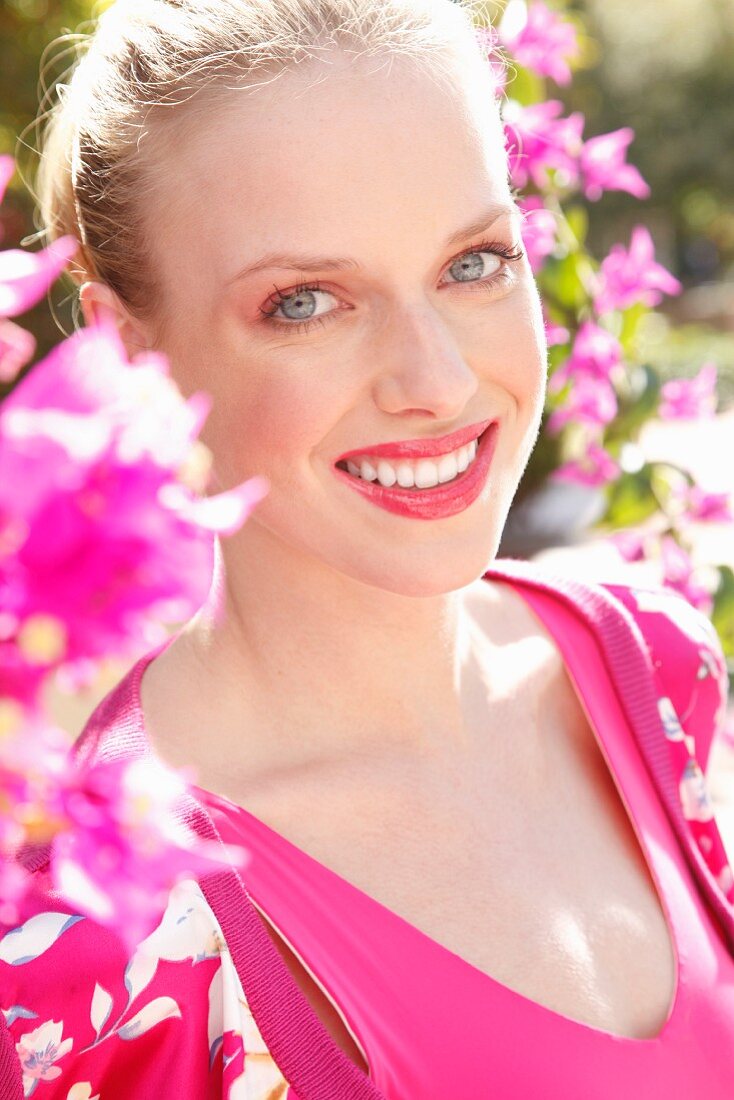 Blonde Frau in pinkfarbenem Top und Cardigan hinter Blumenstrauch