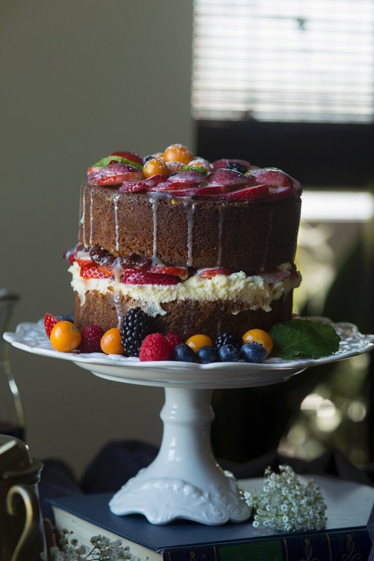 A vanilla cake decorated with fresh fruit on a cake stand