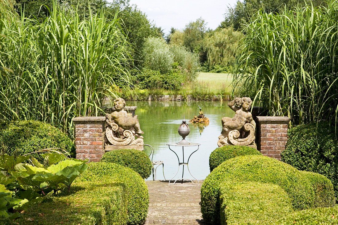 Path lined with box hedges and flanked by angel statues leading to lake