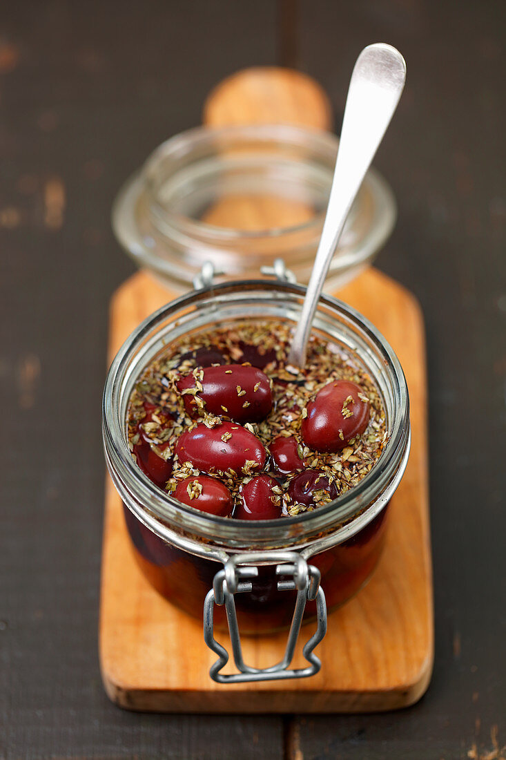 Pickled kalamata olives with oregano in glass jar on a chopping board