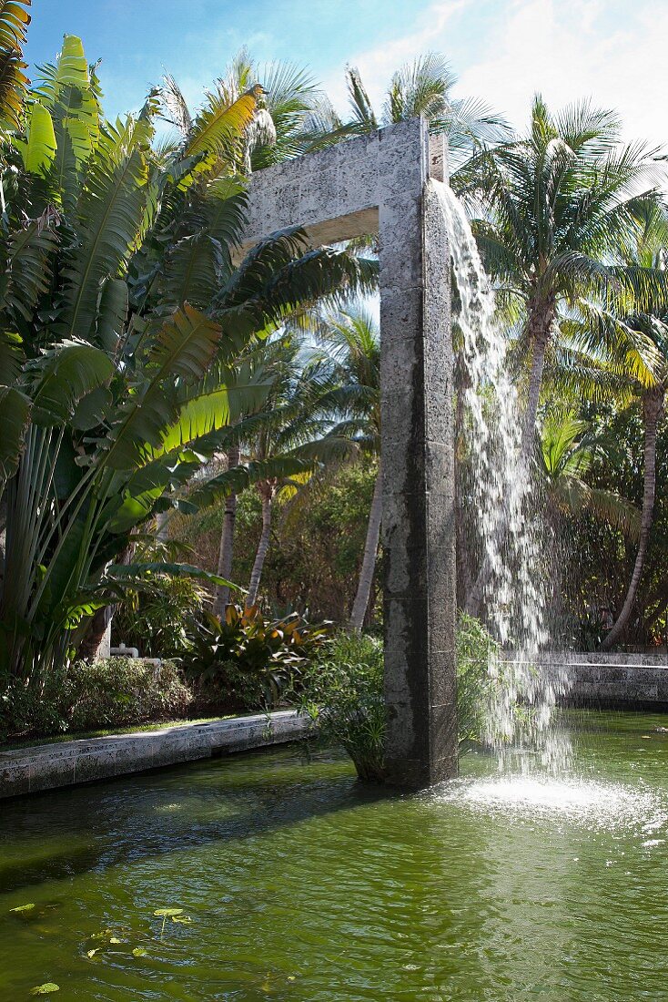 Wasser fällt vom Bogen in einen Brunnen im tropischen Garten