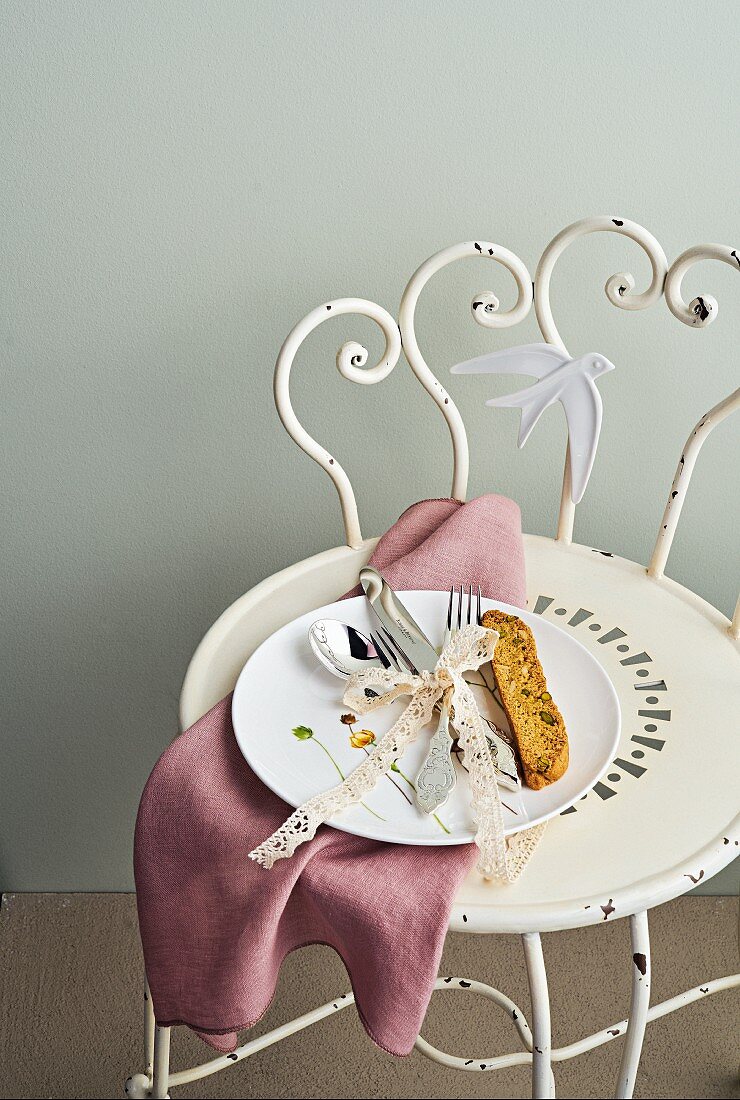East Friesian cutlery tied together with lace ribbon on a porcelain plate on vintage metal chair