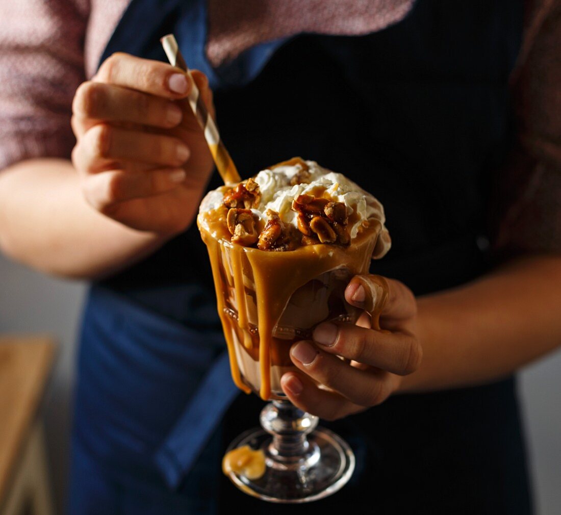 A woman holding a chocolate milkshake with caramel sauce