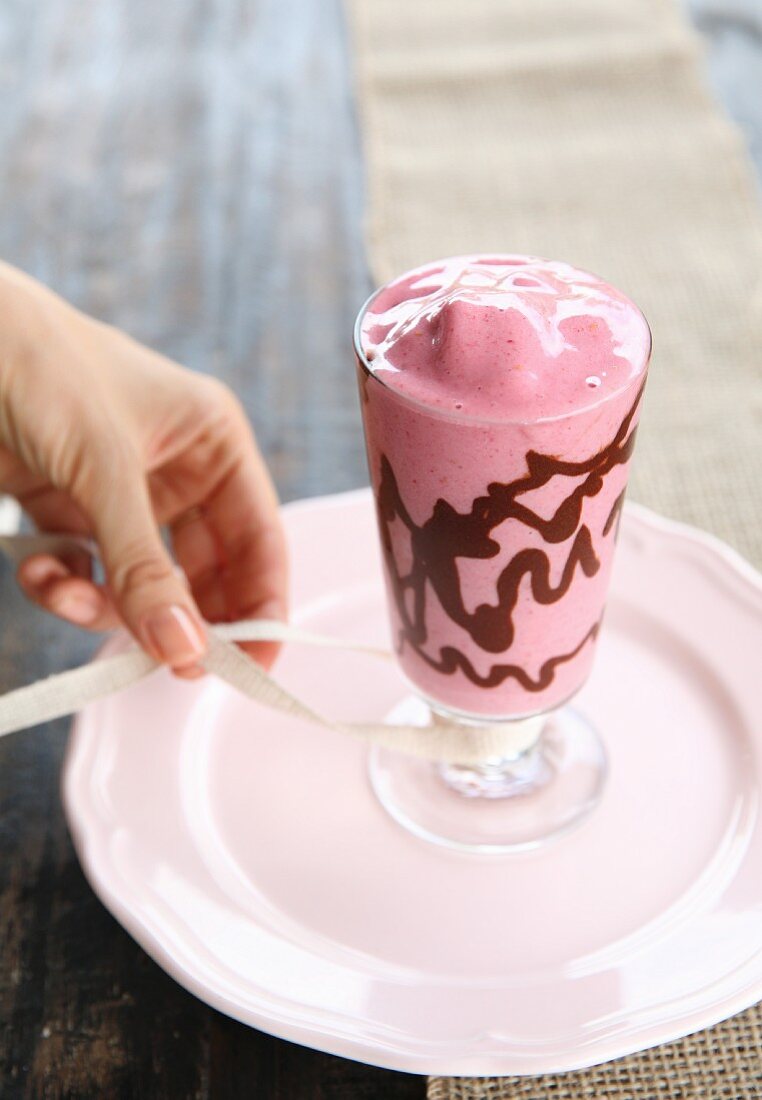 A raspberry and chocolate smoothie in a glass being decorated with ribbon