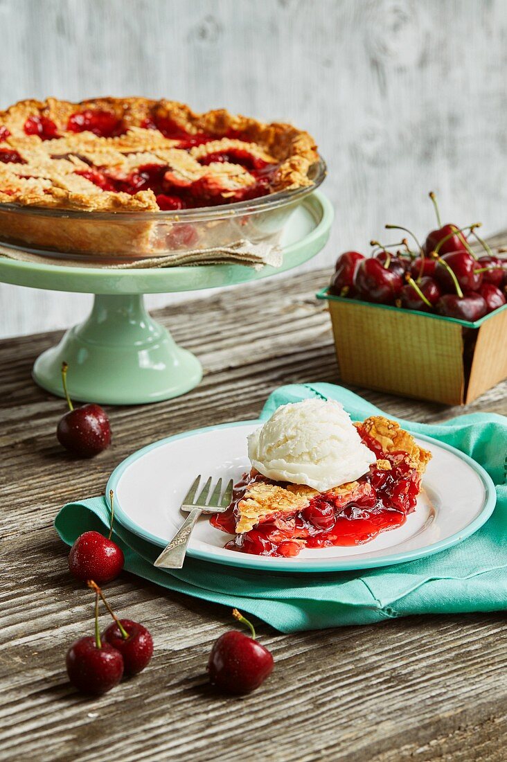 Cherry pie with a lattice top on a cake stand and on a plate with vanilla ice cream