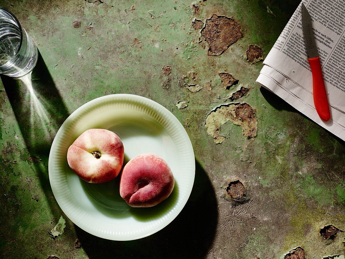 Peaches on a plate next to a newspaper and fruit knife