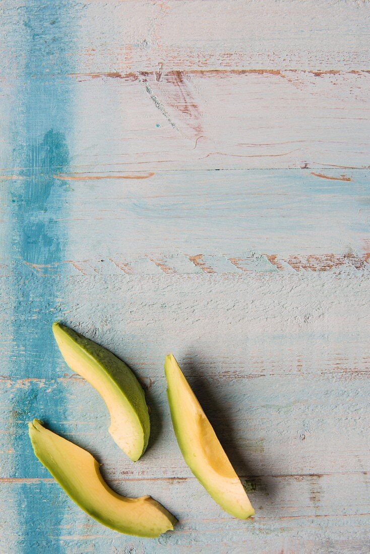 Three wedges of avocado on a wooden surface