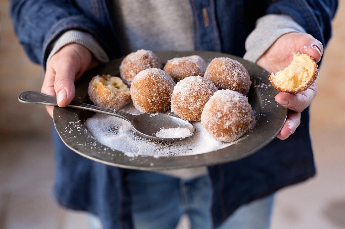 Hände halten rustikalen Zinnteller mit gezuckerten Quarkbällchen