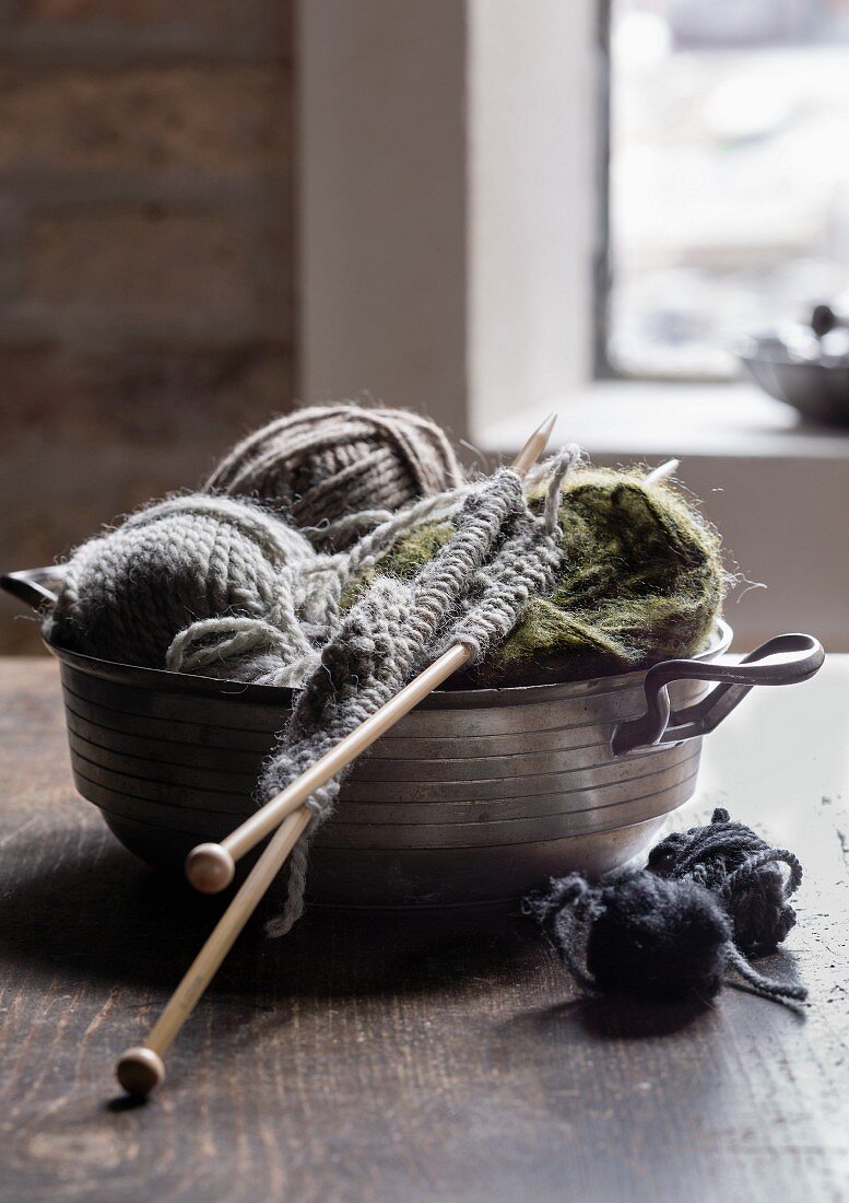 Knitting work and balls of wall in pewter bowl