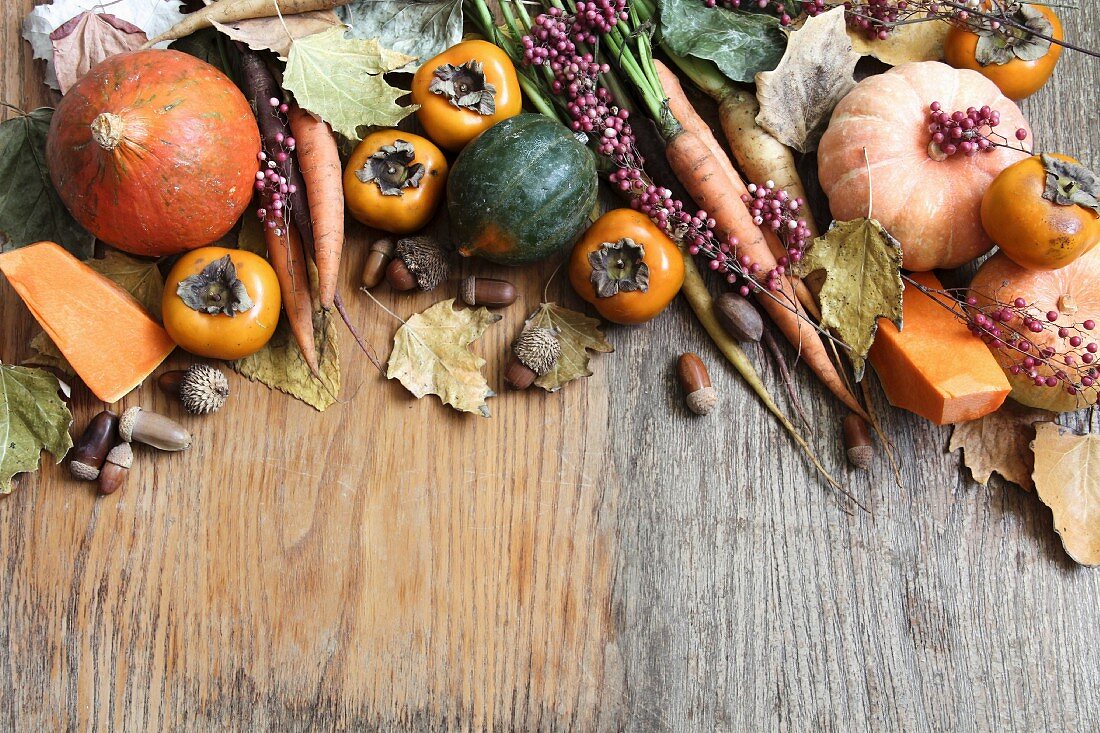 Assorted varieties of autumn vegetables and Japanese persimmon on a wooden surface