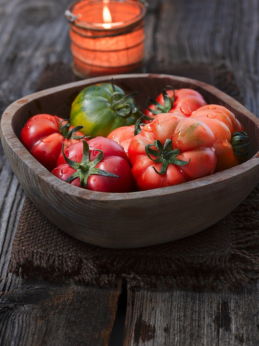 Tomatoes in a wooden bowl in front of a lit candle