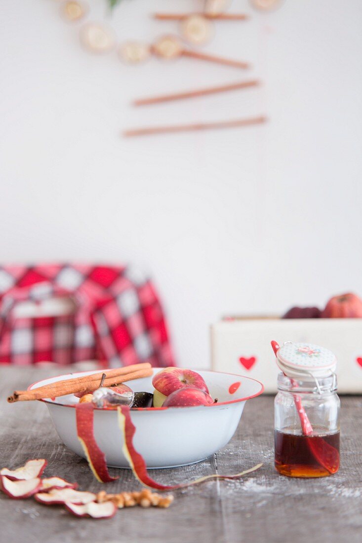 Getrocknete Apfelscheiben, Schüssel mit Zimtstange und Apfelschale und Honigglas auf Holztisch
