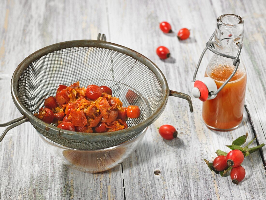 Rose hip juice in a bottle with pitted and boiled rose hips in a strainer