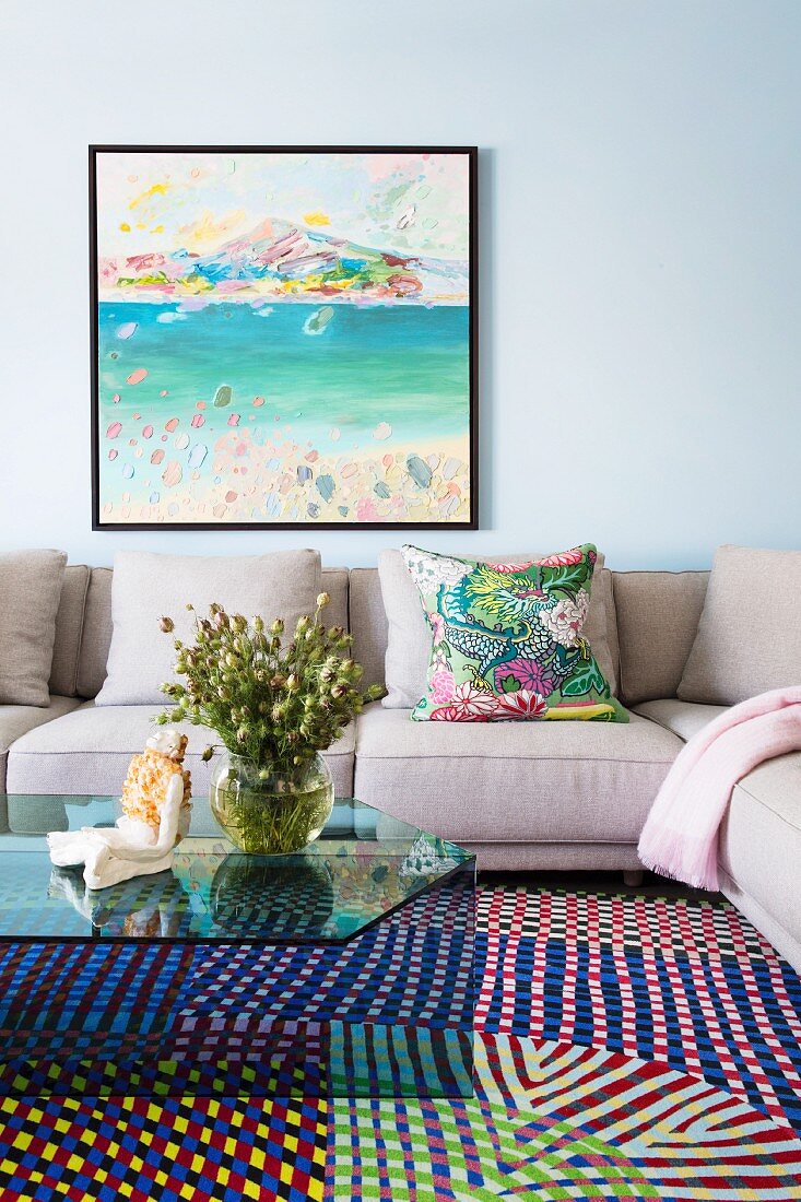 Gray corner sofa with glass coffee table on carpet with colorful geometric patterns