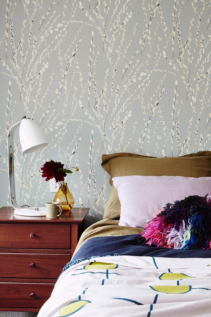 Bed with various textiles in front of a floral patterned wall