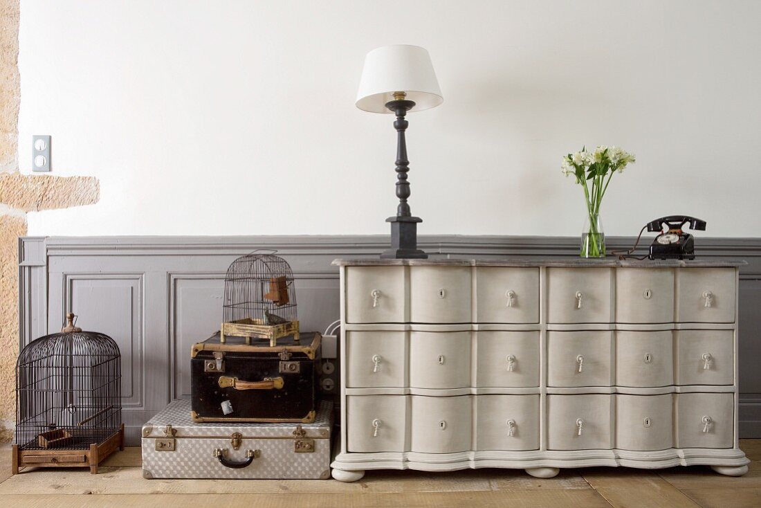 Table lamp on vintage chest of drawers, stacked trunks and birdcages in living room